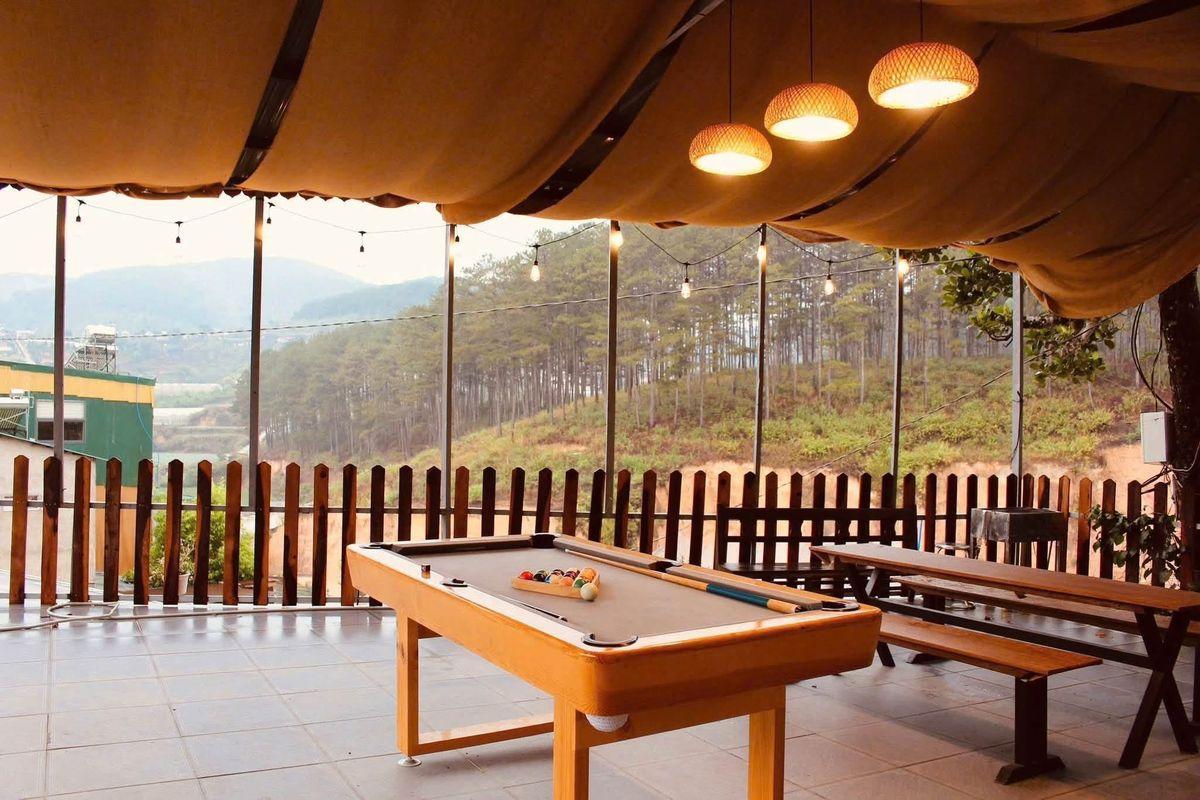 Bàn bida mini đặt ở sân hiên có mái che của quán cafe, nhìn ra đồi thông
